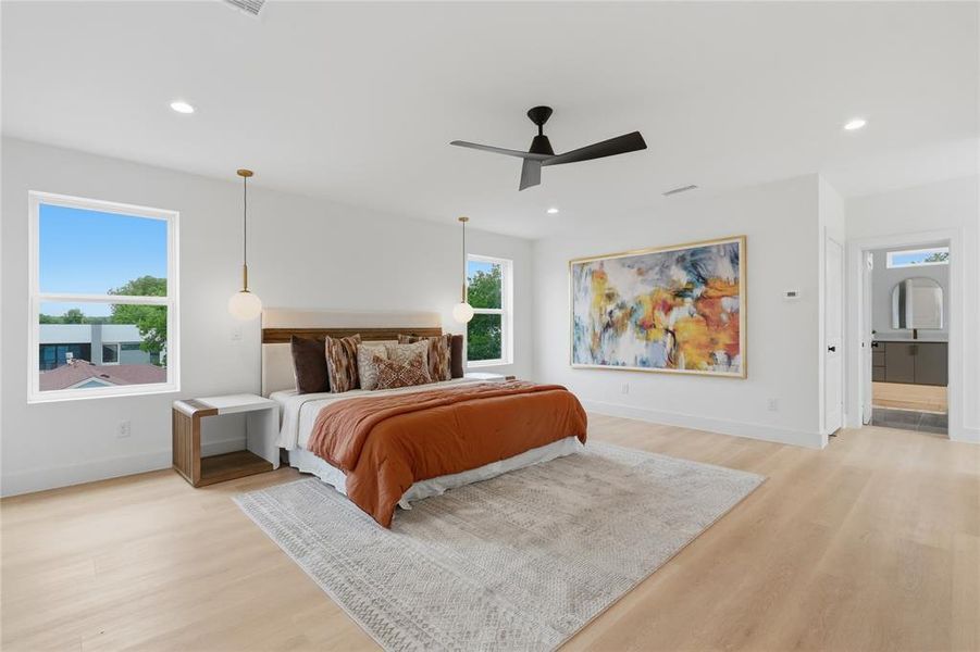 Spacious bedroom featuring light wood-finish flooring, two large windows, a black ceiling fan, recessed lighting, and dual pendant fixtures Spacious bedroom featuring light wood-finish flooring, two large windows, a black ceiling fan, recessed lighting, and dual pendant fixtures