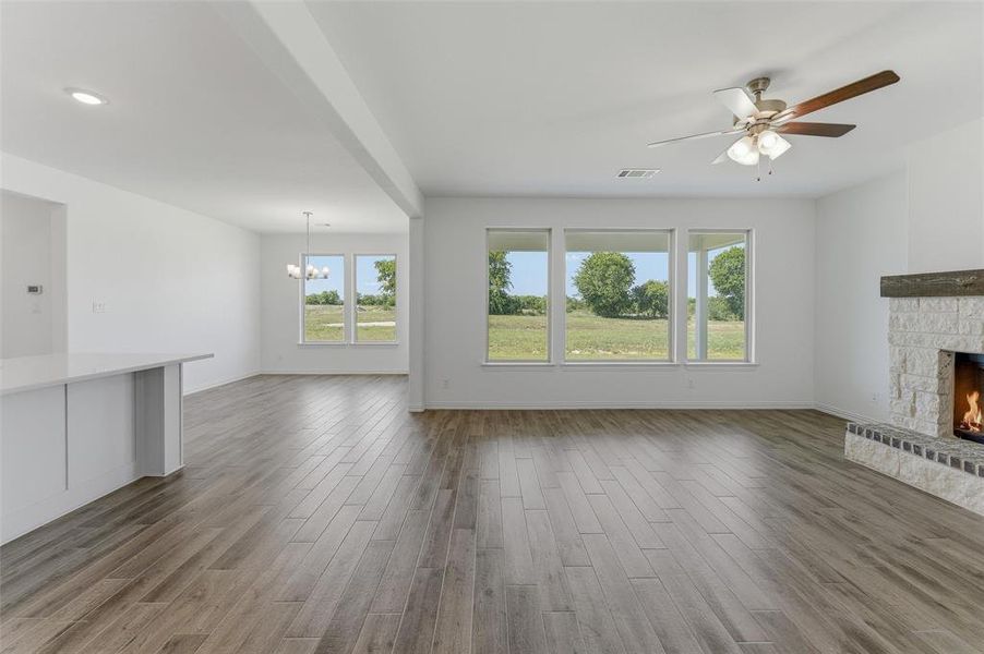 Open-concept living space featuring wood-finish flooring, a stone fireplace with a substantial mantle, and multiple large windows overlooking exterior scenery