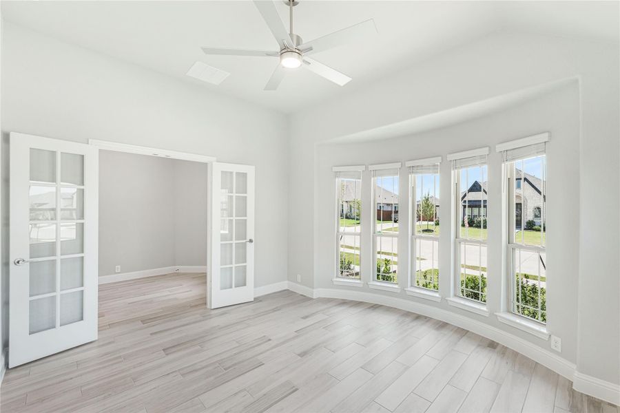Bright empty room with French doors, ceiling fan, large windows, and light wood-look floors
