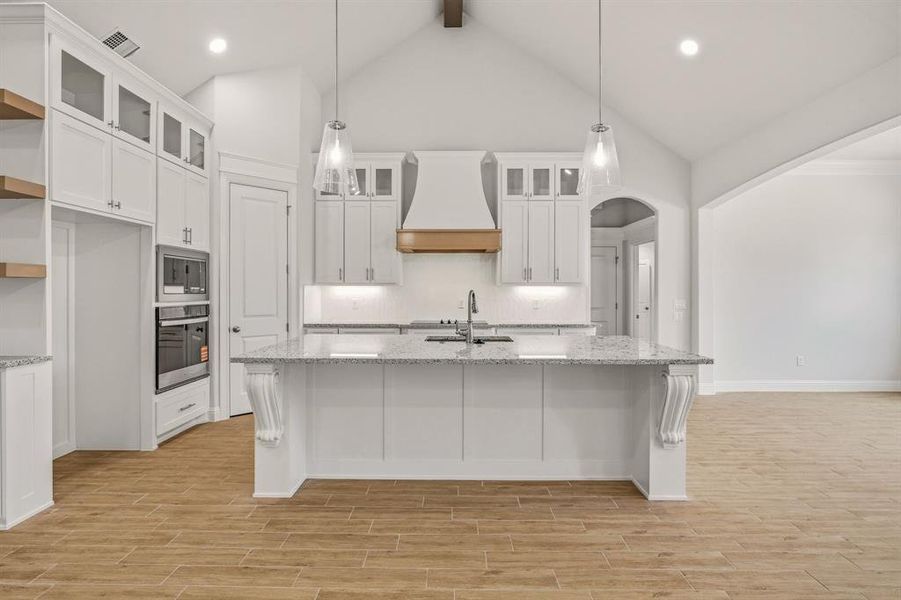 Kitchen with white cabinets, light stone countertops, a kitchen island with sink, and wood finish floors Kitchen with white cabinets, light stone countertops, a kitchen island with sink, and wood finish floors