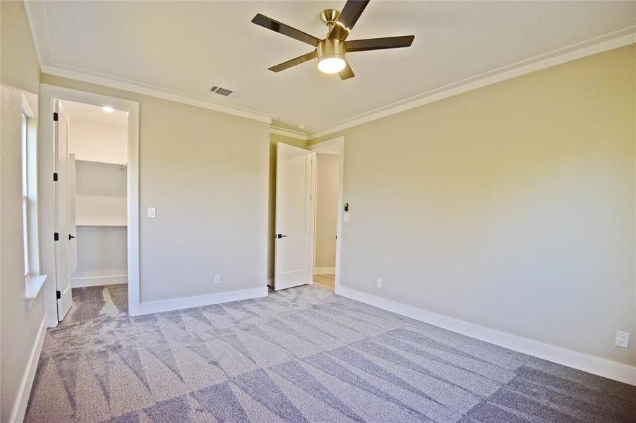 Unfurnished bedroom with light carpet, a walk in closet, ornamental molding, ceiling fan, and a closet