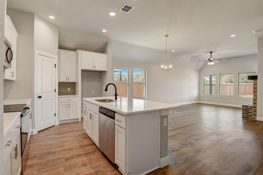 Kitchen with an island with sink, stainless steel appliances, light wood-type flooring, pendant lighting, and ceiling fan with notable chandelier