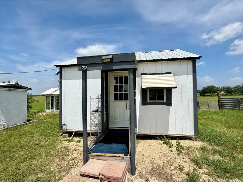 A charming tiny home with white siding and a durable metal roof, set against a wide-open rural landscape.