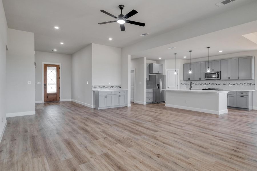 Unfurnished living room featuring light wood finished floors, recessed lighting, a ceiling fan, baseboards, and a sink