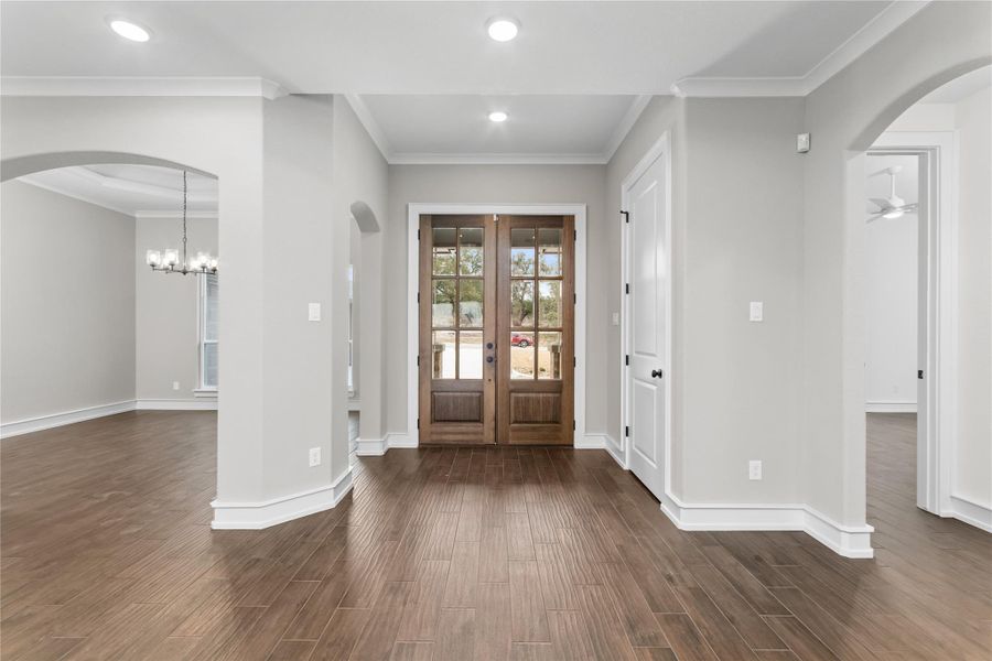 Entrance foyer featuring dark wood-type flooring, arched walkways, french doors, baseboards, and crown molding Entrance foyer featuring dark wood-type flooring, arched walkways, french doors, baseboards, and crown molding
