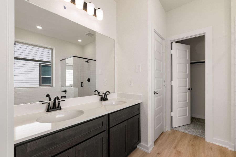 Step into the spa-inspired primary bathroom, a bright and serene sanctuary. This beautifully appointed space features an expansive dual vanity with pristine dark cabinetry, white countertops, and sleek black matte fixtures. A large, frameless mirror runs the length of the vanity, enhancing the sense of light and space. Step into the spa-inspired primary bathroom, a bright and serene sanctuary. This beautifully appointed space features an expansive dual vanity with pristine dark cabinetry, white countertops, and sleek black matte fixtures. A large, frameless mirror runs the length of the vanity, enhancing the sense of light and space.