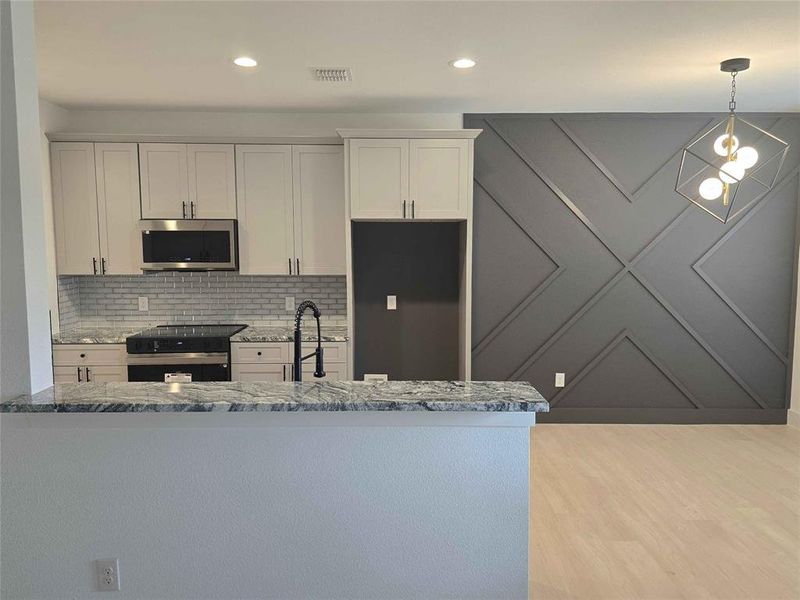 Kitchen with stainless steel appliances, backsplash, granite counters, decorative light fixtures, and cool grey cabinets