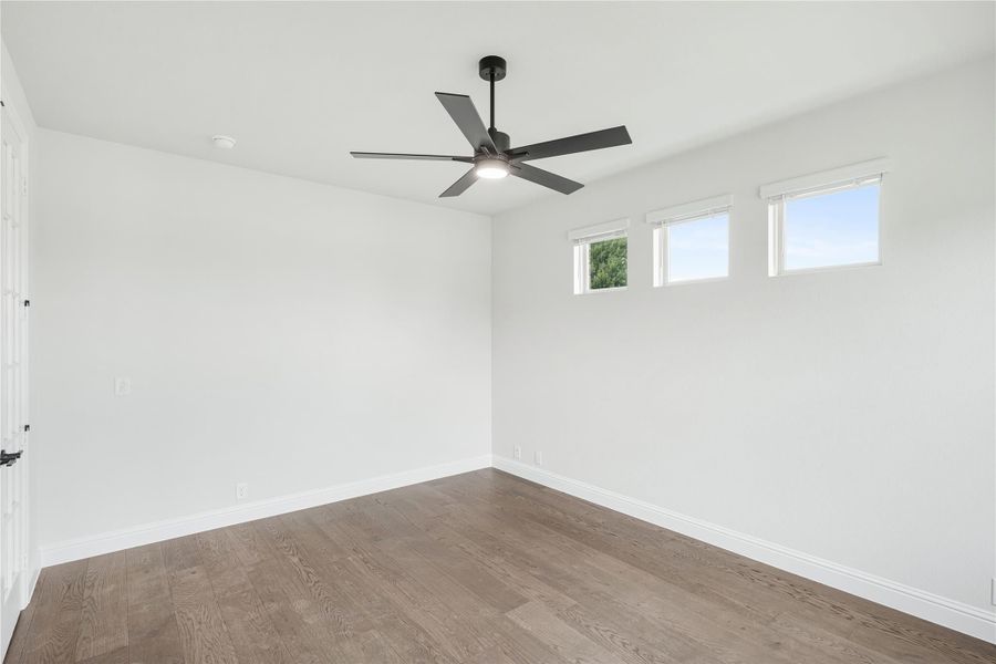 Empty bedroom with hardwood floors, ceiling fan, and two small windows on white walls Empty bedroom with hardwood floors, ceiling fan, and two small windows on white walls