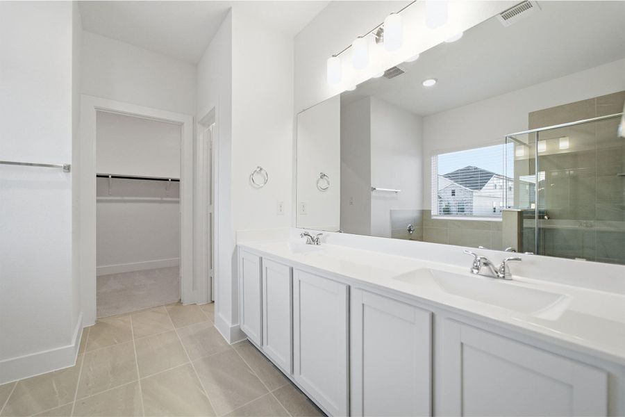 Bathroom with double vanity, a shower stall, light tile patterned floors, and a spacious closet
