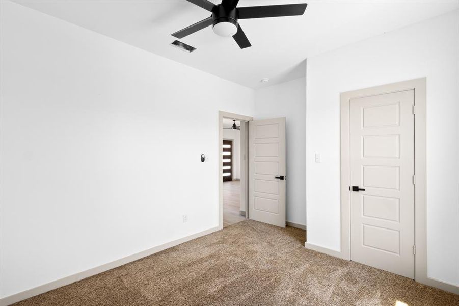 Unfurnished bedroom with visible vents, carpet flooring, and a ceiling fan Unfurnished bedroom with visible vents, carpet flooring, and a ceiling fan