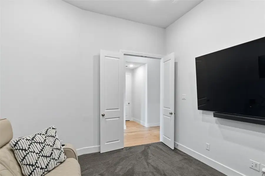 Room featuring a wall-mounted flat screen and soundbar, double entry doors, high ceilings, and dark carpet flooring Room featuring a wall-mounted flat screen and soundbar, double entry doors, high ceilings, and dark carpet flooring
