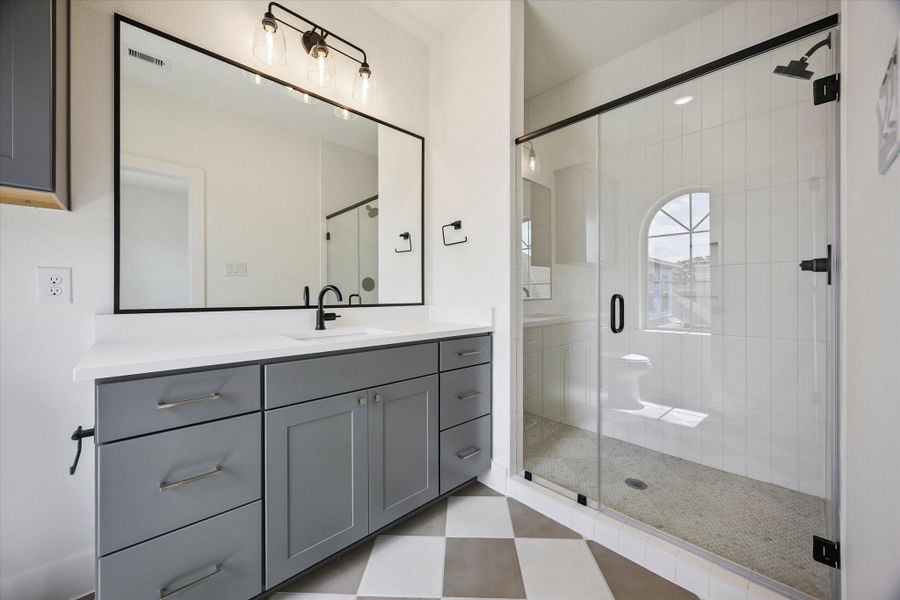 One of the secondary bathrooms with a beautiful floor-to-ceiling tiled glass-enclosed shower and trendy checkered tiled flooring