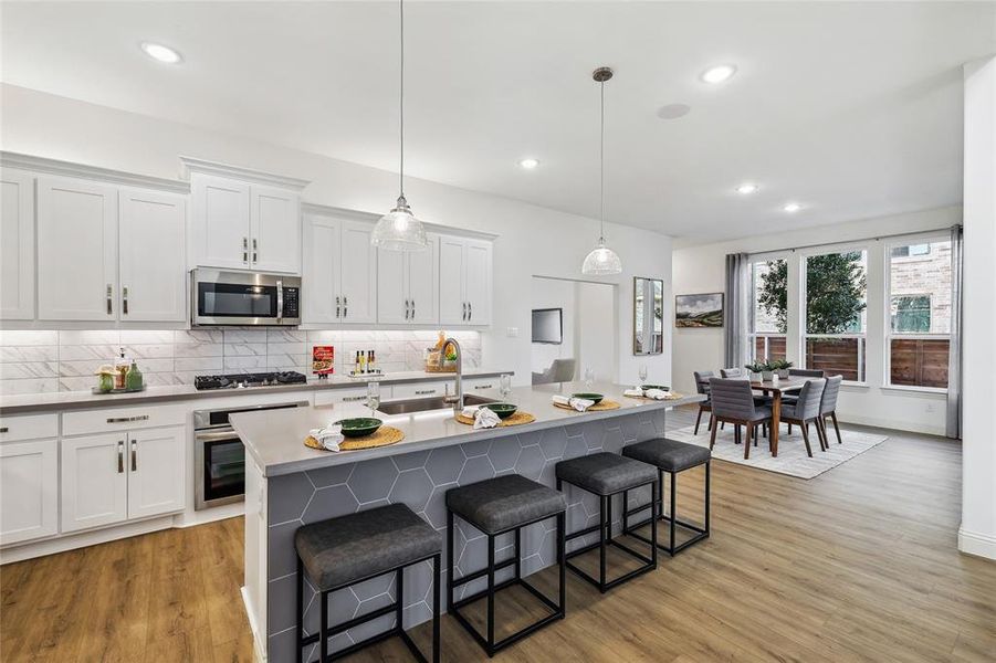 Contemporary open-concept kitchen and dining area featuring white cabinetry, stainless steel appliances, a kitchen island with hexagonal tile detailing, and wood-finish flooring throughout