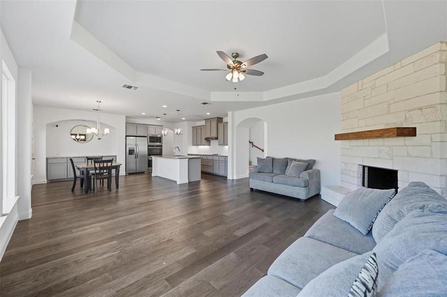 Living area featuring arched walkways, a raised ceiling, dark wood-type flooring, a stone fireplace, and a chandelier