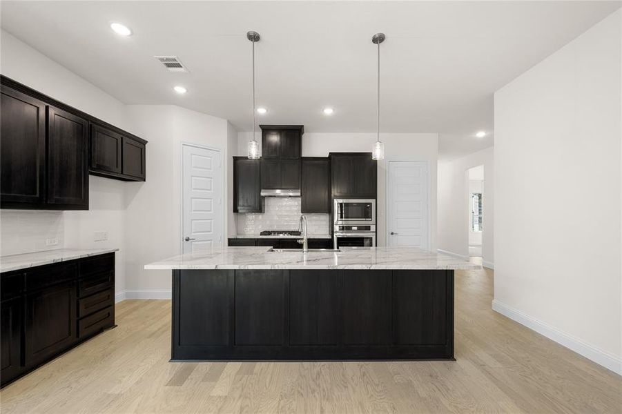 Kitchen with stainless steel appliances, light wood-style floors, decorative backsplash, light stone counters, and recessed lighting