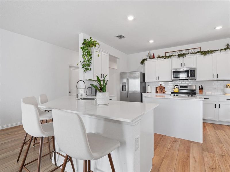 Kitchen featuring a kitchen bar, white cabinetry, appliances with stainless steel finishes, and light hardwood / wood-style flooring