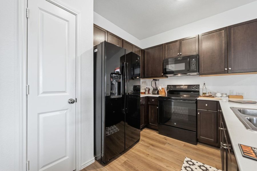 Full kitchen featuring dark wood-finish cabinetry, light countertops, and wood-finish flooring