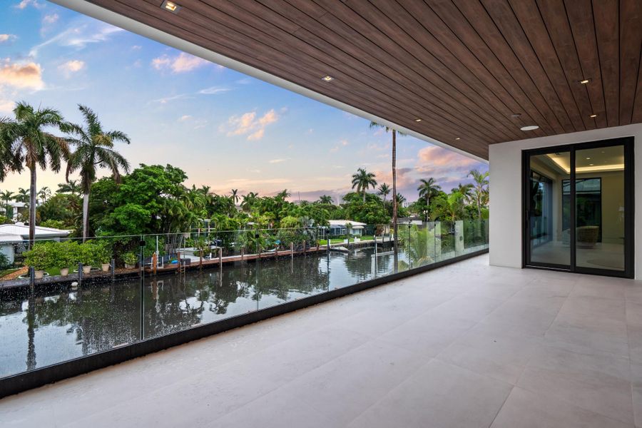 Expansive covered balcony with wood-accent ceiling and glass railings showcasing tranquil canal and sunset views. Expansive covered balcony with wood-accent ceiling and glass railings showcasing tranquil canal and sunset views.