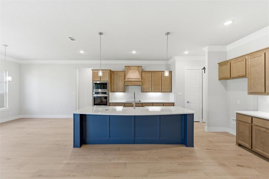 Kitchen featuring crown molding, light wood finished floors, an island with sink, light stone countertops, and stainless steel appliances