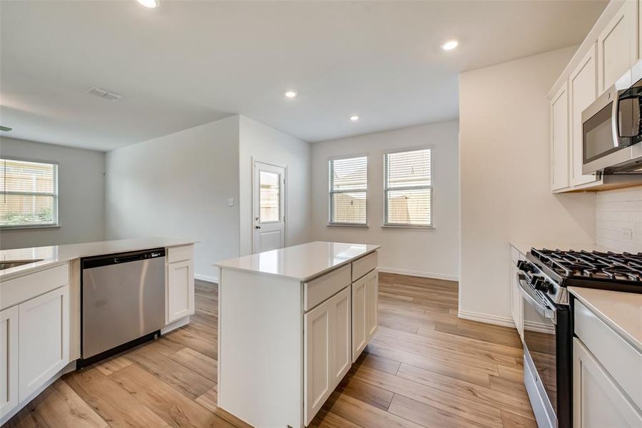 Kitchen featuring tasteful backsplash, stainless steel appliances, light wood-type flooring, a kitchen island, and white cabinets