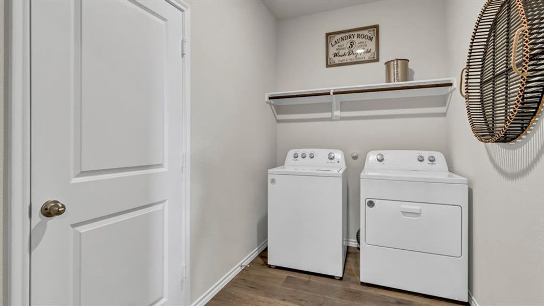 Dedicated laundry area featuring a white door with brass hardware, wood-finish flooring, and a wall-mounted shelf above the appliances Dedicated laundry area featuring a white door with brass hardware, wood-finish flooring, and a wall-mounted shelf above the appliances