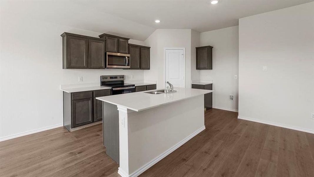 Kitchen featuring wood-finish flooring, dark wood cabinetry, stainless steel appliances, a center island with an integrated sink, and recessed lighting