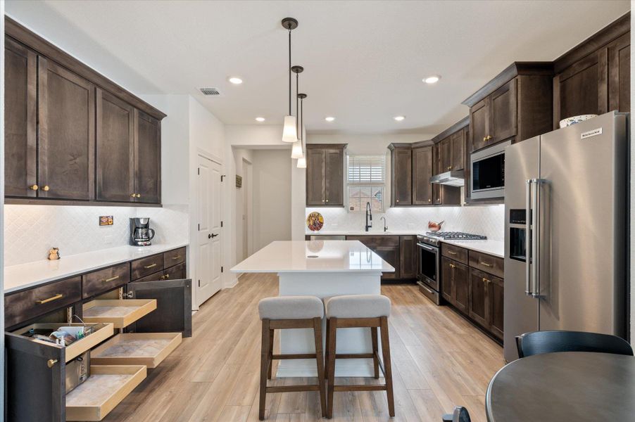 Kitchen with dark wood finish cabinetry, high end appliances, a kitchen island, and light wood finished floors Kitchen with dark wood finish cabinetry, high end appliances, a kitchen island, and light wood finished floors