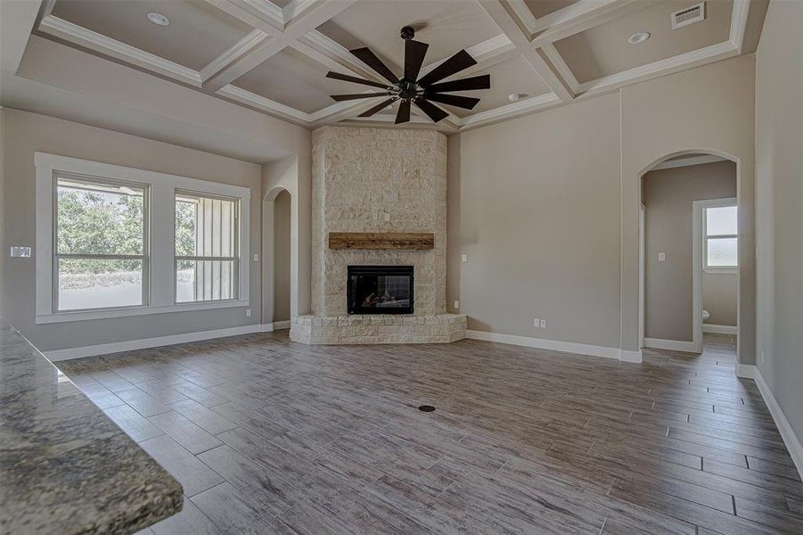 Unfurnished living room featuring coffered ceiling, ceiling fan, beam ceiling, and a stone fireplace