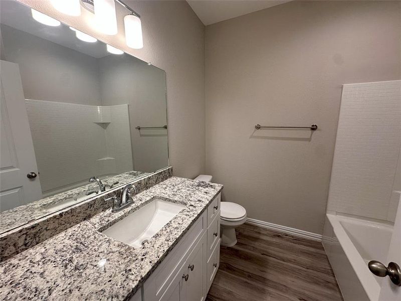 Full bathroom with hardwood / wood-style floors, toilet, bathing tub / shower combination, and vanity