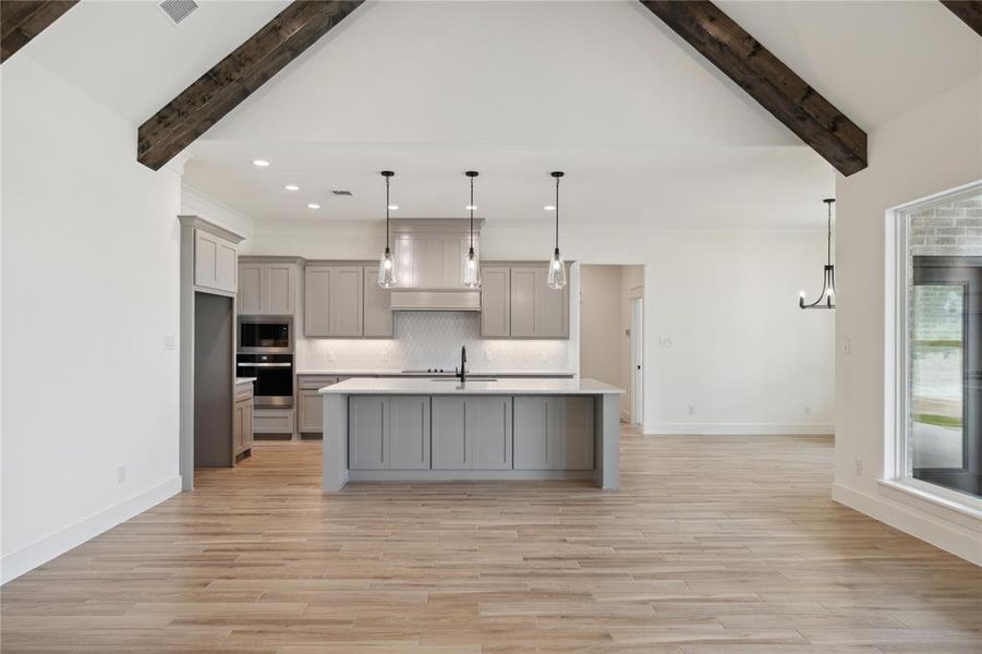 Kitchen with vaulted ceiling with beams, gray cabinetry, a center island with sink, and light hardwood / wood-style flooring