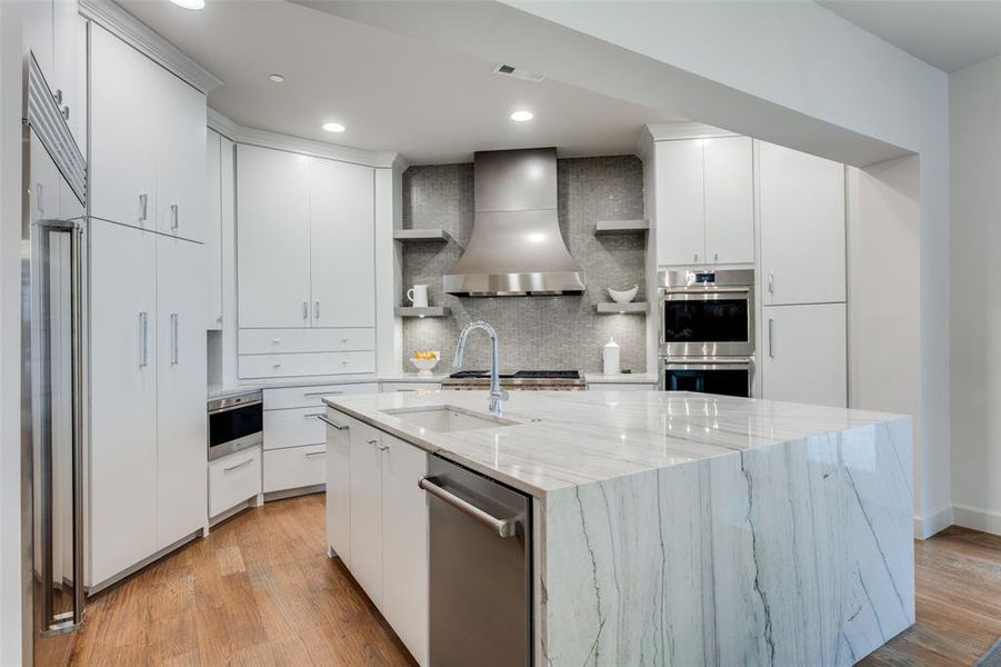 Kitchen with white cabinetry, wall chimney range hood, stainless steel appliances, decorative backsplash, and light hardwood / wood-style floors