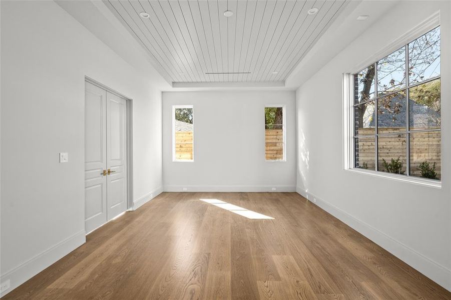 One of two primary suites, the downstairs bedroom offers a spacious and serene retreat. Large windows bring in natural light and provide peaceful backyard views, while the rich white oak hardwood floors enhance the warmth of the space. A painted tongue-and-groove ceiling with recessed lighting adds architectural interest, making this suite a refined and inviting haven.