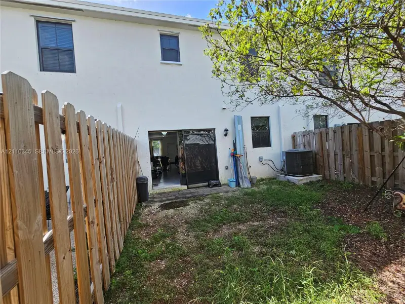 Fenced outdoor space featuring a paved patio area and mature trees