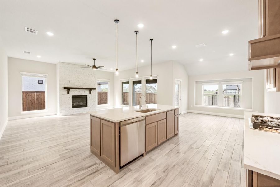 Open kitchen with center island, pendant lights, and stone fireplace in connected living area