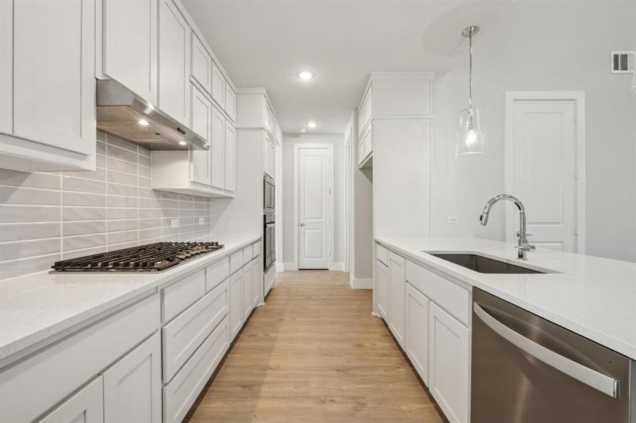 Kitchen featuring pendant lighting, sink, stainless steel appliances, white cabinets, and light wood-type flooring