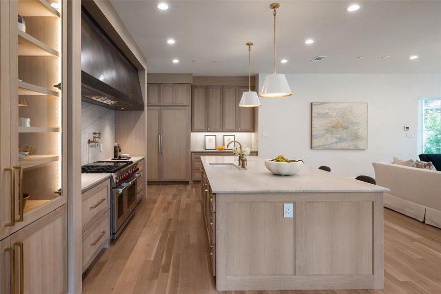 Kitchen featuring light wood-type flooring, sink, range with two ovens, and a kitchen island with sink