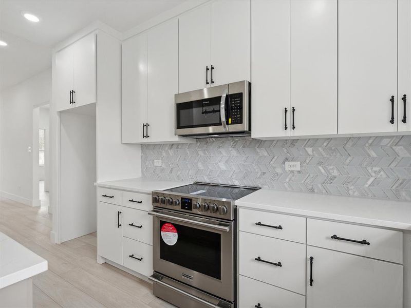 Kitchen with decorative backsplash, white cabinets, stainless steel appliances, and light wood-type flooring