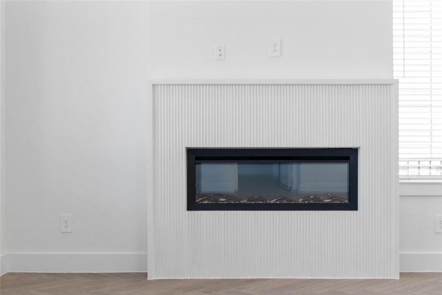 The fireplace serves as the modern, sophisticated centerpiece of the Great Room, featuring a sleek linear electric insert set within a striking fluted white surround. This architectural detail provides a rich, rhythmic texture that draws the eye and adds a contemporary layer to the room’s clean aesthetic.