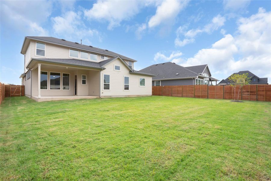 A spacious, verdant yard extends behind a contemporary home, featuring a covered patio and full privacy fencing. A spacious, verdant yard extends behind a contemporary home, featuring a covered patio and full privacy fencing.