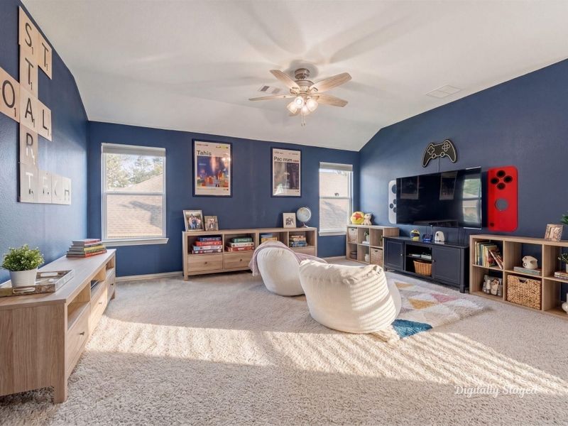 Generously sized bonus room with bold navy accent walls, a vaulted ceiling, and a ceiling fan. Carpeted and full of natural light, it offers flexible space for a game room, media lounge, or recreation area. This photo has been digitally staged to illustrate the possibilities of the home's aesthetic and potential design. Some furnishings and décor shown are for visual inspiration.