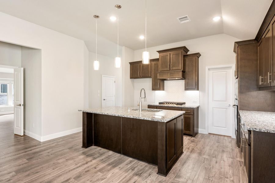 Kitchen with dark wood cabinets, granite island with sink, pendant lights, and light hardwood floors