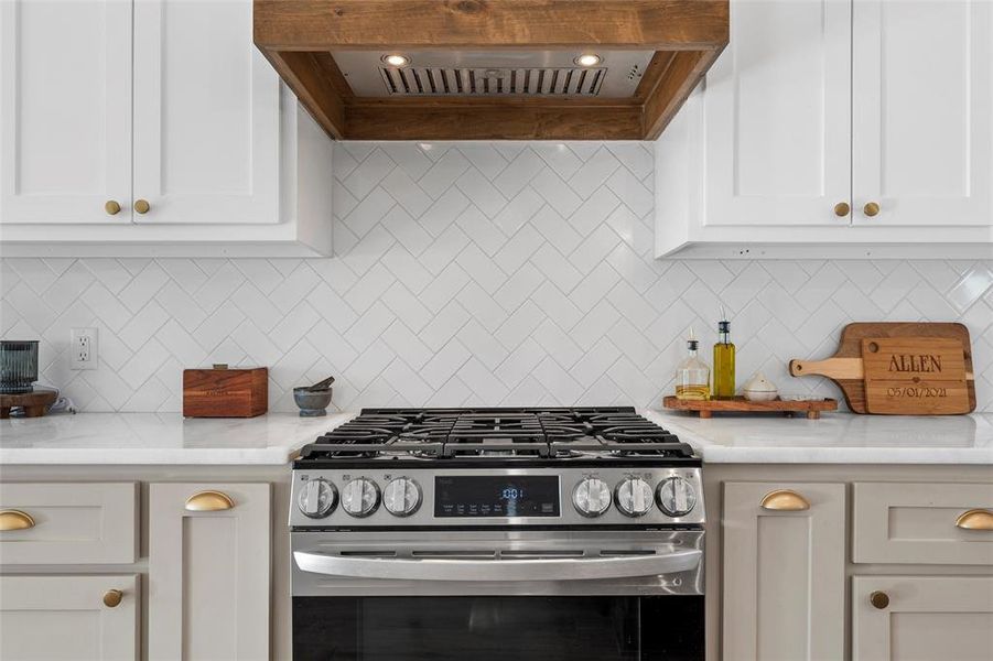 Kitchen featuring ventilation hood, stainless steel gas range, white cabinets, and tasteful backsplash