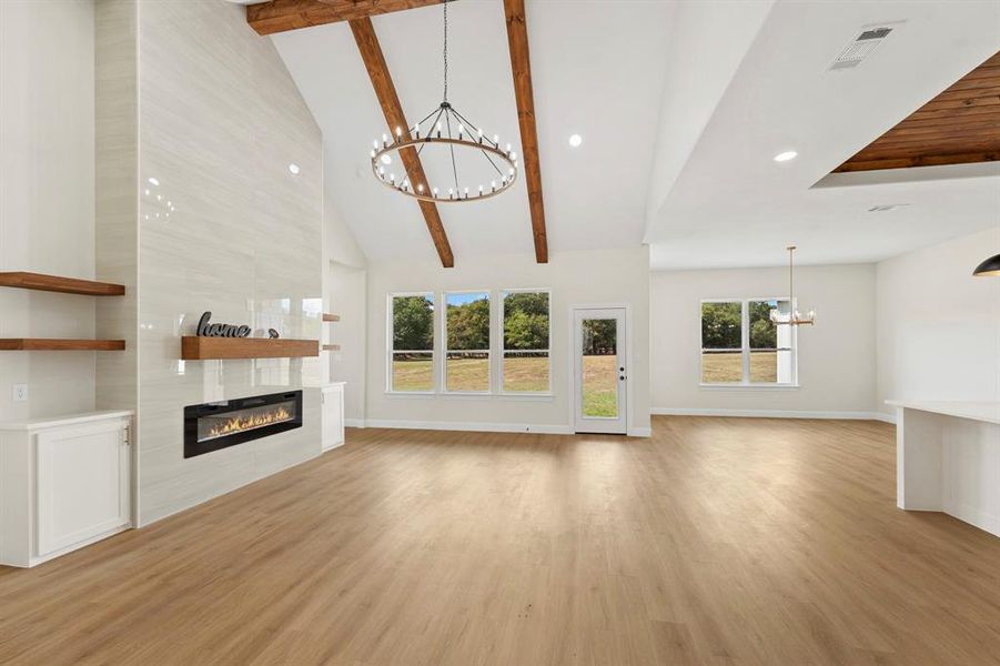 Unfurnished living room featuring a chandelier, beamed ceiling, a fireplace, light wood-type flooring, and high vaulted ceiling