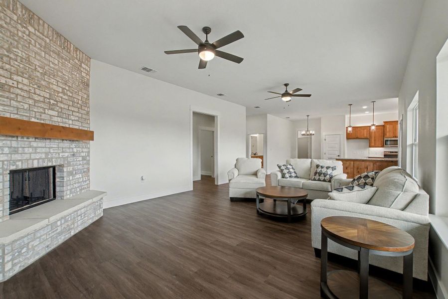 Living room with suspended lighting, dark wood finished floors, a fireplace, and ceiling fan