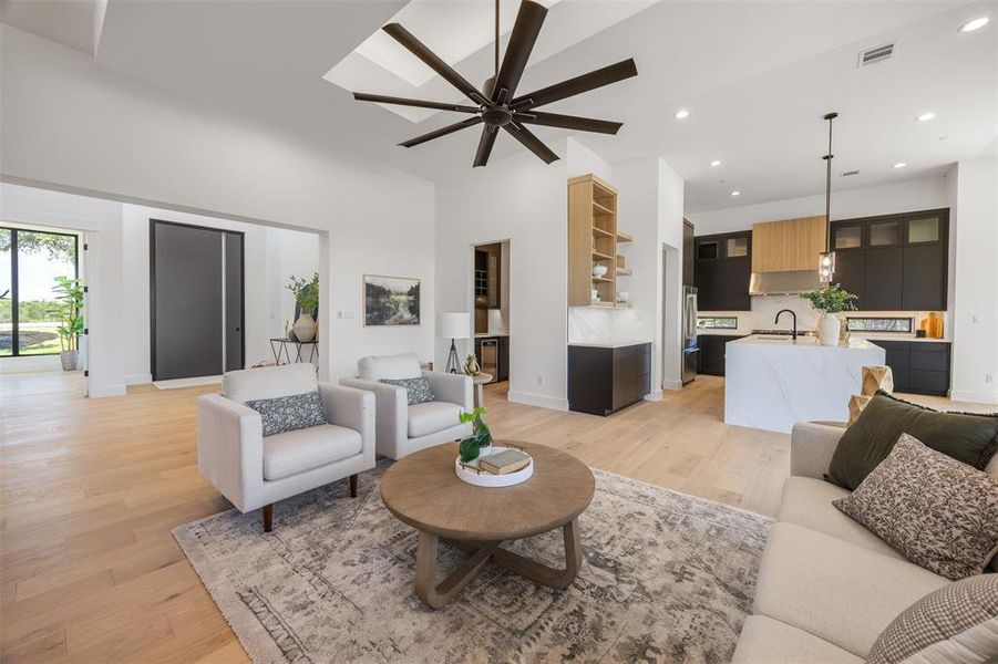An open-concept living area boasts a chef's kitchen, high ceilings, and light hardwood flooring.