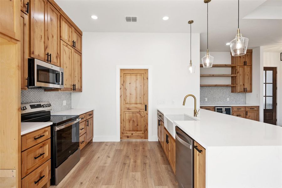 Kitchen with a peninsula, stainless steel appliances, brown cabinetry, decorative light fixtures, and light stone countertops