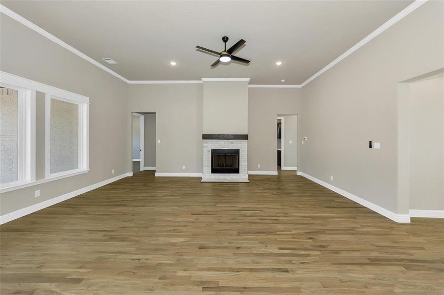 Unfurnished living room featuring crown molding, light wood-style floors, a brick fireplace, recessed lighting, and a ceiling fan