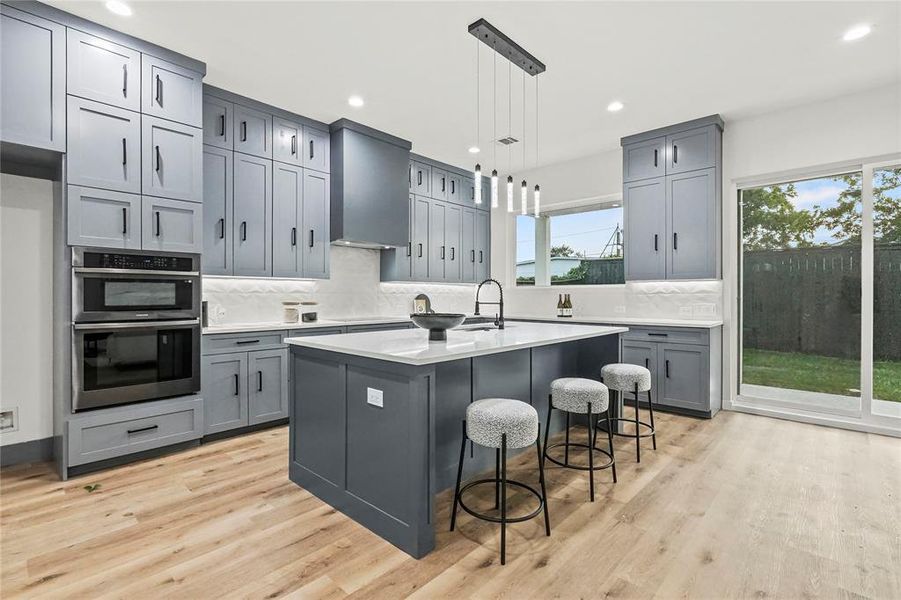 Kitchen featuring decorative backsplash, light hardwood / wood-style flooring, stainless steel double oven, and a wealth of natural light