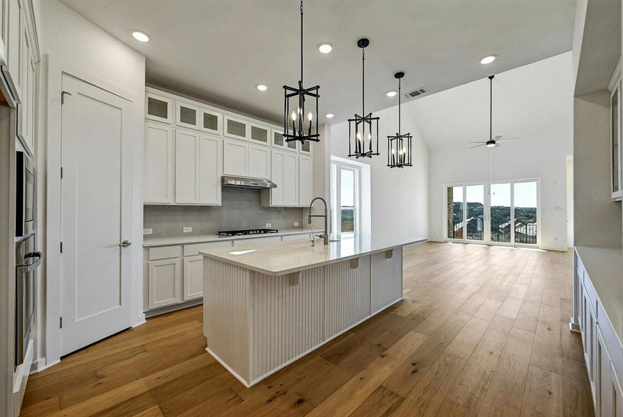Kitchen featuring a chandelier, light countertops, high vaulted ceiling, light wood-style flooring, and under cabinet range hood
