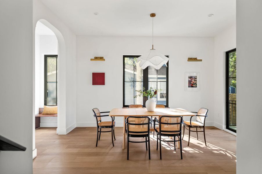 Naturally illuminated dining space features warm wood flooring and an elegant hanging fixture, creating an inviting atmosphere.